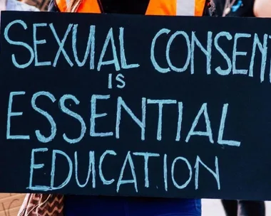 Protester holding a sign that reads, "Sexual consent is essential education," during a march.