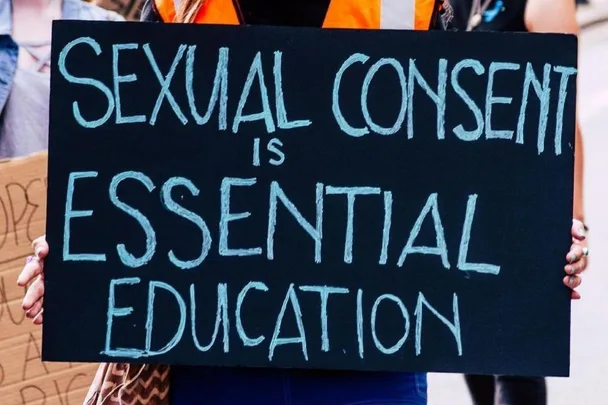 Protester holding a sign that reads, "Sexual consent is essential education," during a march.