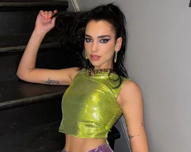 Singer wearing a shimmering green top, posing on stairs.