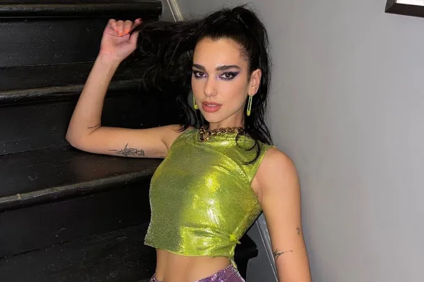 Singer wearing a shimmering green top, posing on stairs.