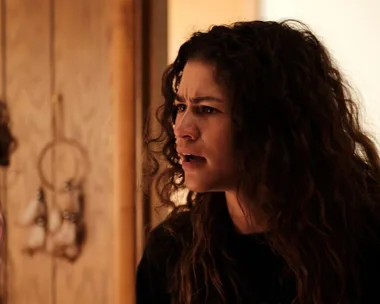 A character in "Euphoria" with curly hair looks intense and emotional in a warmly-lit room.