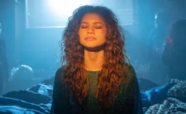 Rue from "Euphoria" stands with closed eyes in a blue-lit room, wearing a sparkly green top.