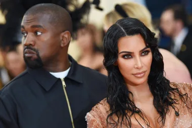 Two people at a formal event, one looking away, the other facing forward with wavy hair and wearing a shimmering outfit.