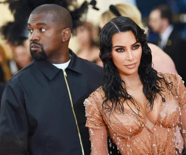 A man in a dark jacket looks to the side, while a woman in a sparkling, nude-toned dress poses confidently.