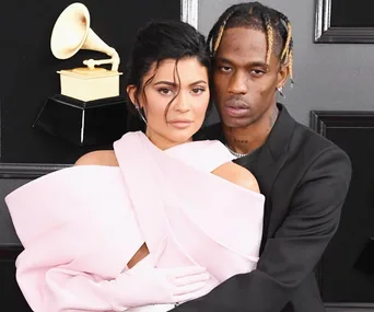 A couple poses at an event in formal attire, with a Grammy award visible in the background.