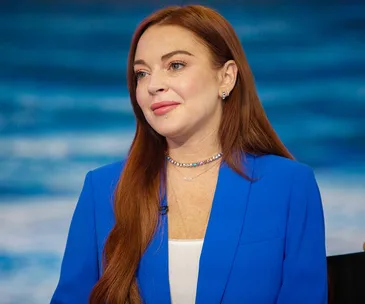 A person with long red hair wearing a blue blazer smiles softly against a blurred blue background.