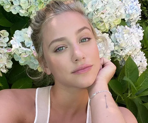 Young woman with blonde hair, resting on white flowers, looking at the camera with a soft expression.