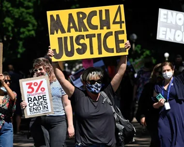 Protesters hold signs, including "March 4 Justice," at a rally advocating against violence and injustice.