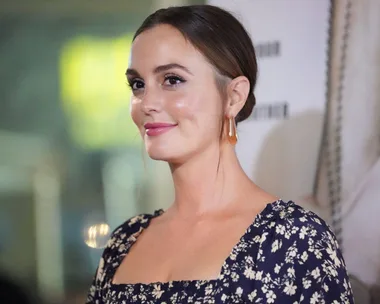 A woman with brown hair in a bun, wearing a floral dress, smiles at an event.