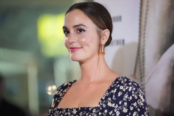 A woman with brown hair in a bun, wearing a floral dress, smiles at an event.