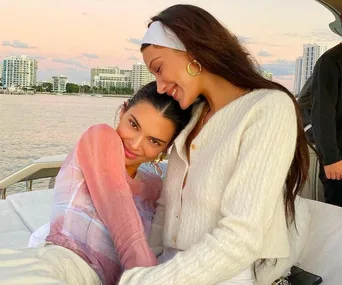 Two women smiling and embracing on a boat at sunset, with city skyline in the background.