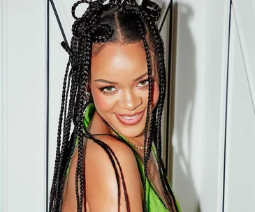 A woman with braided hair smiles, wearing a green outfit against a light background.