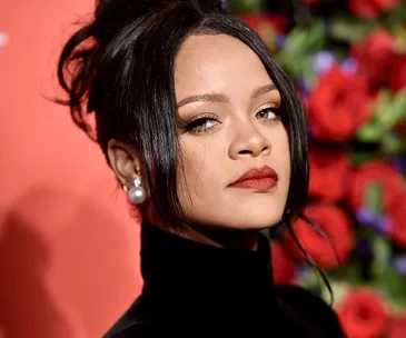 "Rihanna with red lips, elegant updo, pearl earrings against a floral and red backdrop."