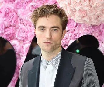 A person in a suit stands in front of a pink floral backdrop.