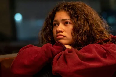 Zendaya as Rue Bennett in Euphoria, wearing a red hoodie, looking thoughtfully to the side.