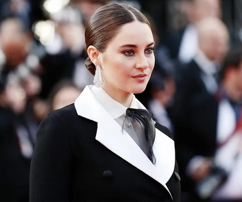 Actor in a black and white suit at a formal event with a blurred crowd in the background.