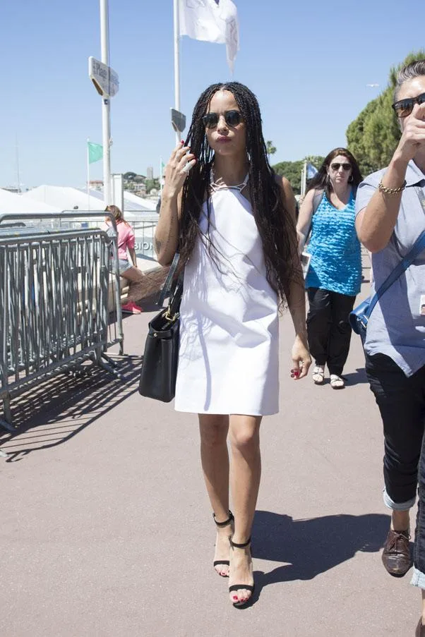 Zoe Kravitz in a white dress and sunglasses walking outdoors on a sunny day.
