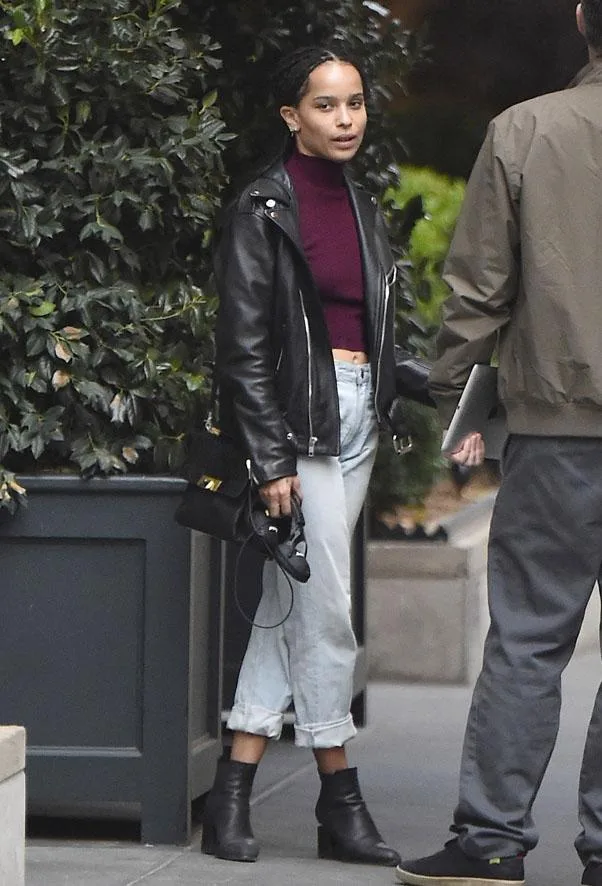 ```plaintext
Person in leather jacket, crop top, jeans, and boots stands next to another person outdoors.
```