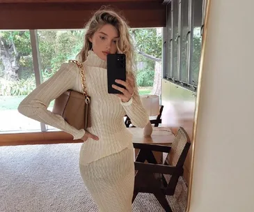 Woman in a cream ribbed outfit taking a mirror selfie with a beige handbag over her shoulder.