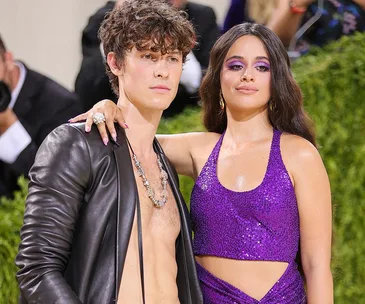 A couple poses together at a formal event, with the woman in a sparkly purple dress and the man in an open leather jacket.