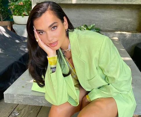 Woman in a green outfit sitting, with her head resting on her hand, in an outdoor setting.