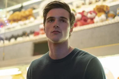 Young man with short dark hair in a casual setting, looking serious, with blurred plush toys in the background.