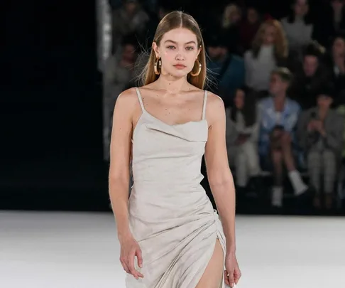 Model walking down the runway in a light, form-fitting dress during a fashion show.