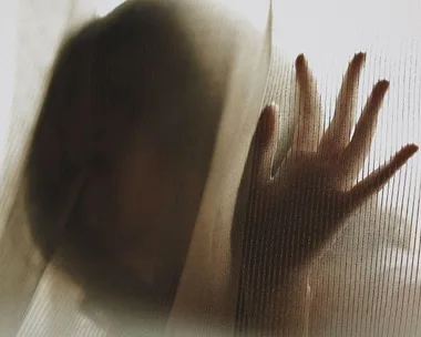 A silhouette of a person with a hand pressed against a translucent curtain.