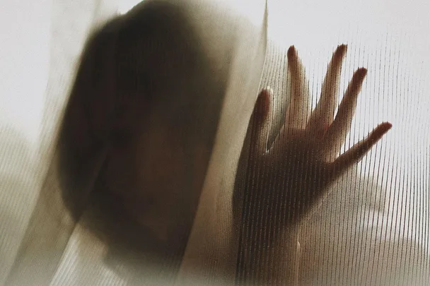 A silhouette of a person with a hand pressed against a translucent curtain.