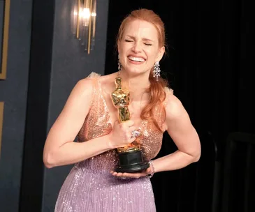 Smiling woman in a pink dress holds an Oscar trophy, celebrating her award win at the 2022 Oscars ceremony.