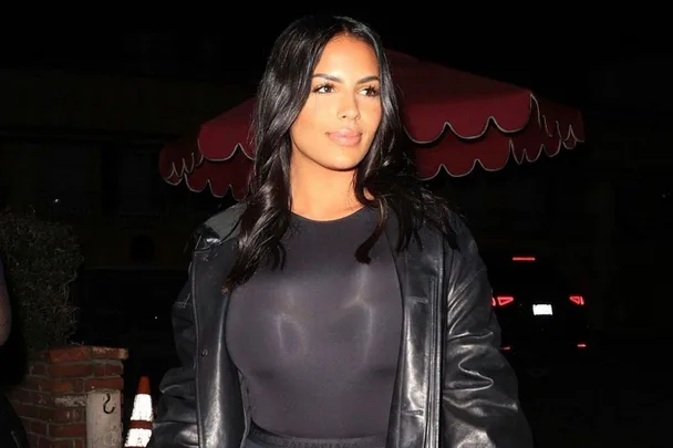 A woman in a black outfit and leather jacket, standing outdoors at night, with a red umbrella in the background.