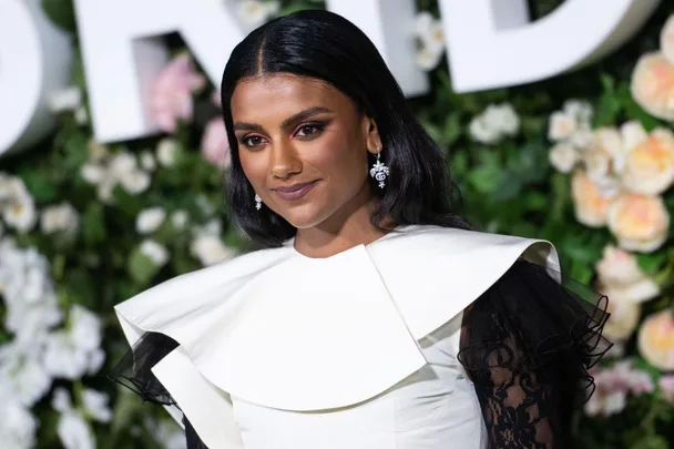 A woman in a white and black dress with floral background, wearing earrings, smiles at an event.