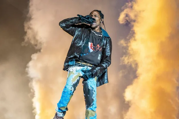 Performer on stage in colorful attire, singing passionately with smoke and flames in the background.