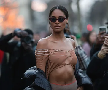 A model in a stylish, revealing top and sunglasses poses amidst photographers, showcasing bold evening fashion.