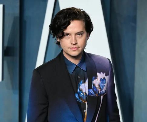 A person in a dark floral suit at a formal event, posing against a stylish blue backdrop.