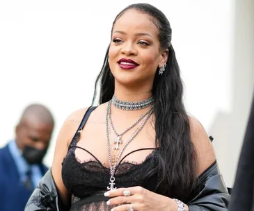 Rihanna wearing a lace bodysuit with layered necklaces and a leather jacket at an event.