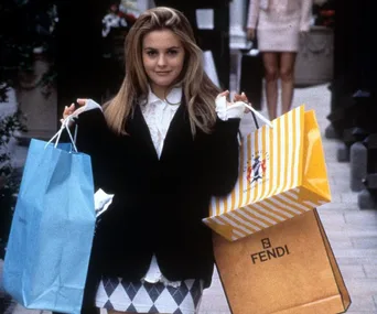 A person holding shopping bags, including a blue one and a yellow Fendi bag, walking down a street in a stylish outfit.