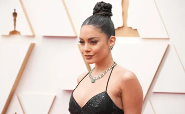 Vanessa Hudgens at a formal event, wearing a black sequin gown, emerald jewelry, and a braided bun hairstyle.