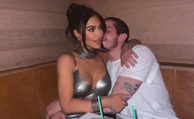 A couple sitting closely in a wooden booth, with drinks on the table. The woman wears a metallic dress.