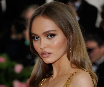 A woman with long hair and gold dress poses at an event, with a blurred crowd in the background.