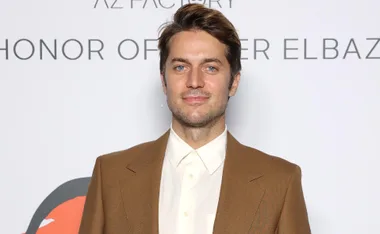 Man in a brown suit with neutral background at an event.