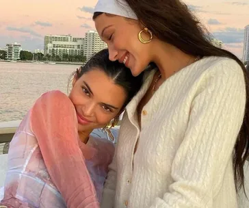 Two women smiling and embracing on a boat with a city skyline at sunset in the background.