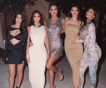 Five women pose together in stylish outfits at a nighttime event.