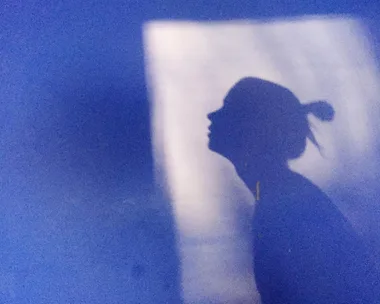 A silhouette of a person in profile against a blue background with light illuminating the shadow.