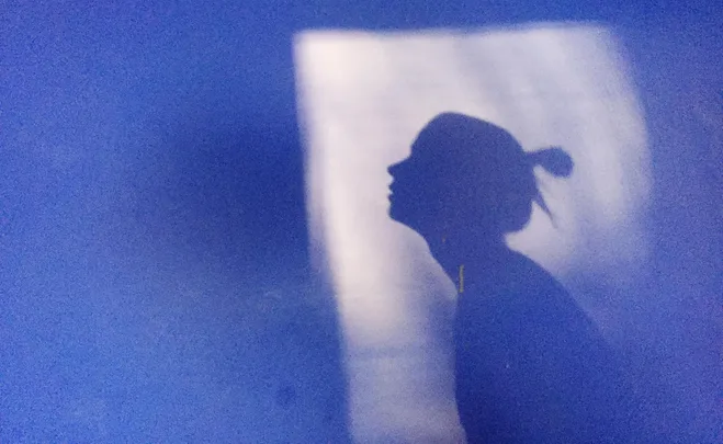 A silhouette of a person in profile against a blue background with light illuminating the shadow.