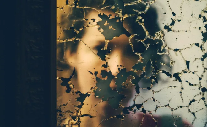 Blurred reflection of a person in a cracked, broken mirror.