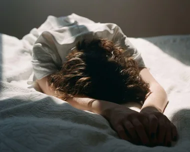 Person lying face-down on a bed, with sunlight streaming in.