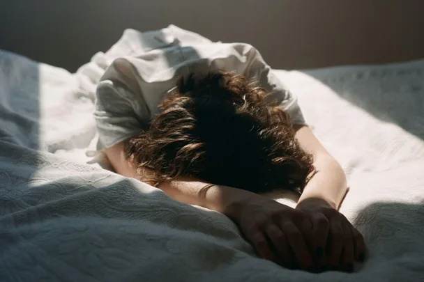 Person lying face-down on a bed, with sunlight streaming in.