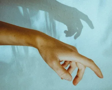 A hand reaching out with its shadow cast on a light blue wall.