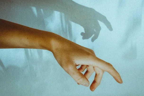 A hand reaching out with its shadow cast on a light blue wall.